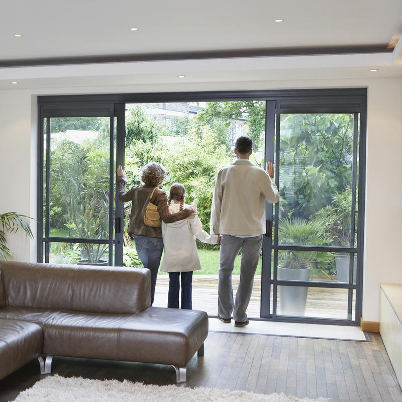 Rear,View,Of,Parents,And,Daughter,Looking,Through,Patio,Door